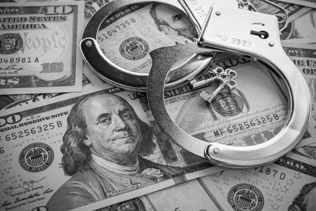 Pair of metal police handcuffs on USD US dollar banknotes money cash background. Corruption, dirty money, gambling or financial crime ideas concept. Monochrome tone.