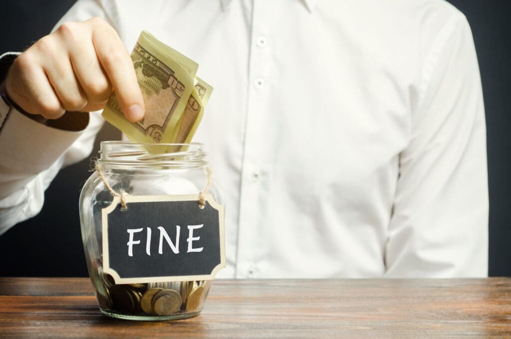 A man puts dollars in a glass jar with the word Fine. Saving money and paying a fine. Punishment for a crime and offense. Financial punishment. Violations of traffic laws. Fraud. Monetary penalty.