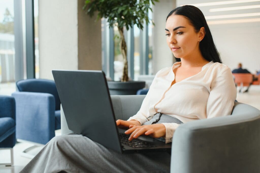 Young businesswoman sitting at sofa and working with laptop at the waiting hall of the business center.