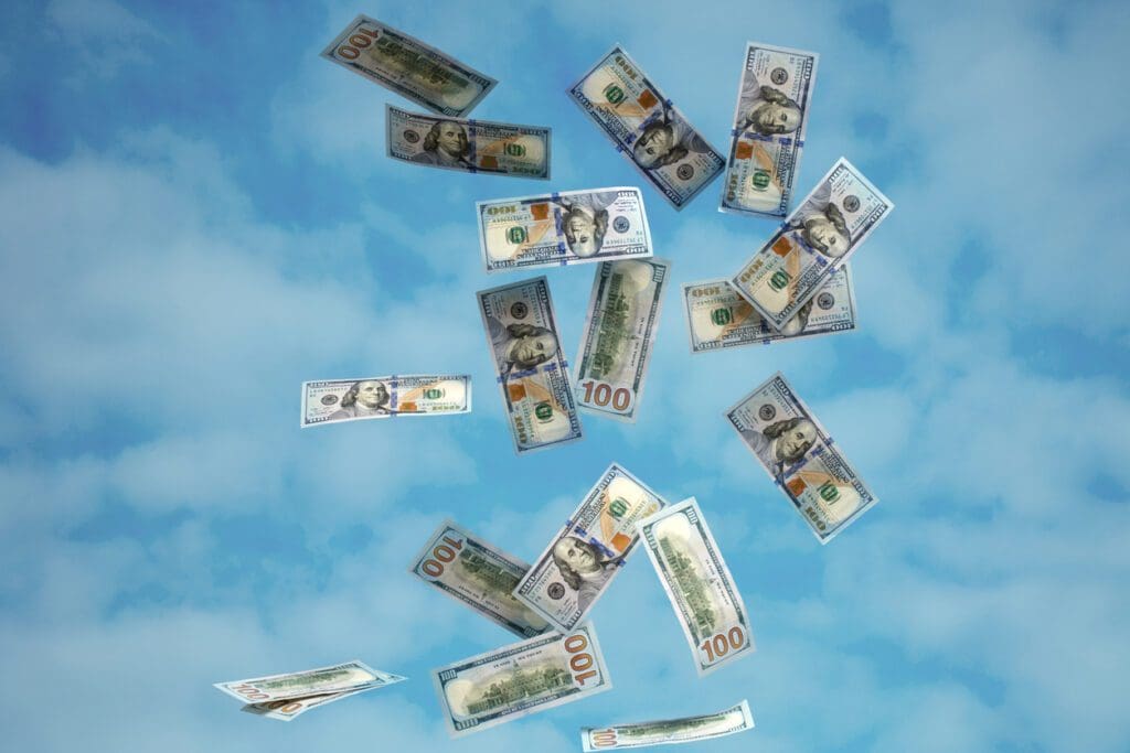 One hundred dollars bills falling (flying) on a blue sky background.